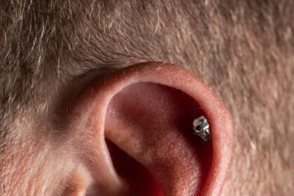 Close-up van een oor met meerdere piercings in de oorlel en het kraakbeen, waaronder een groene steen